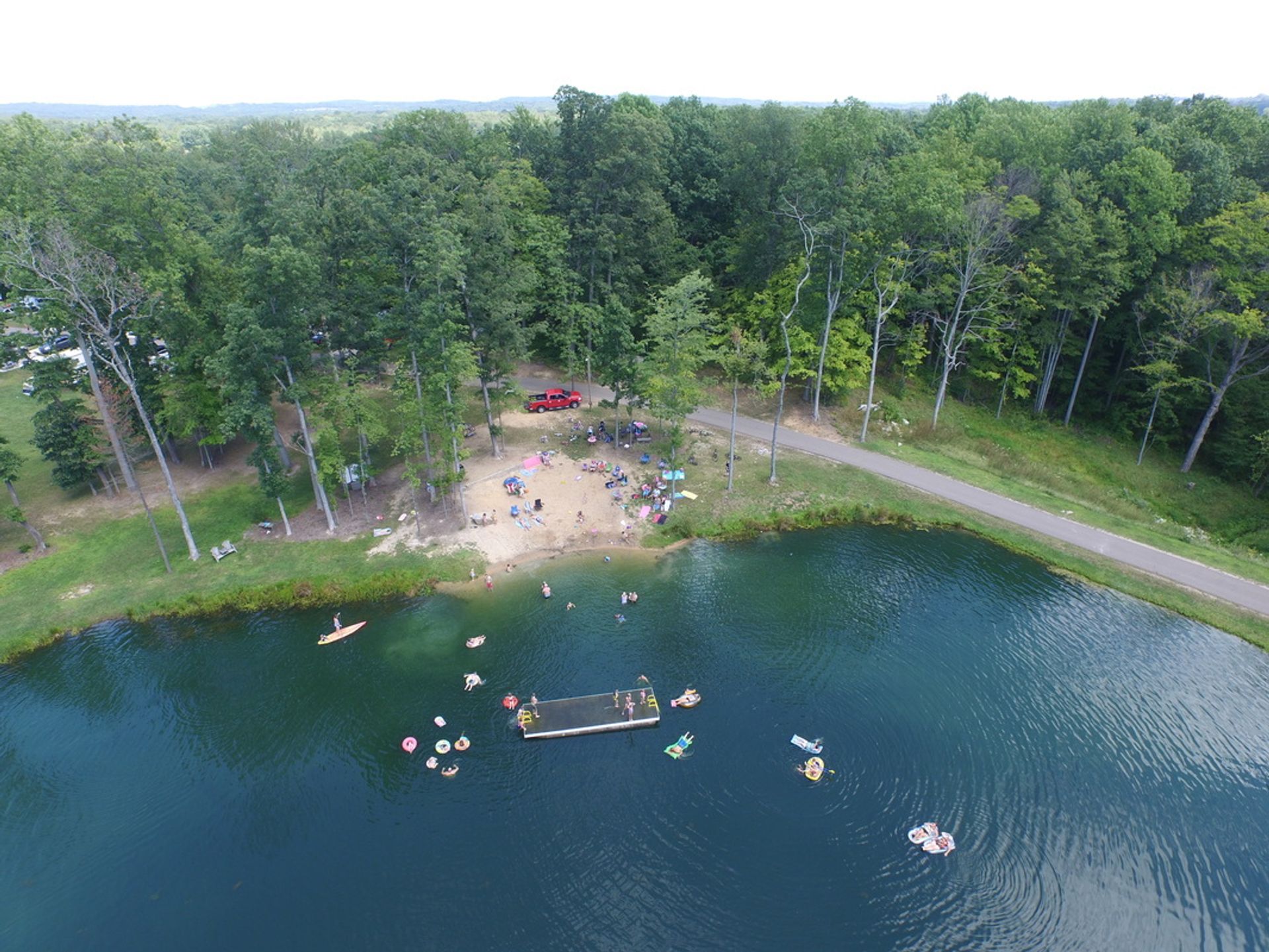 Triponds Family Camp Resort: An aerial view of a serene lake surrounded by trees, with people enjoying various activities on the water and land.