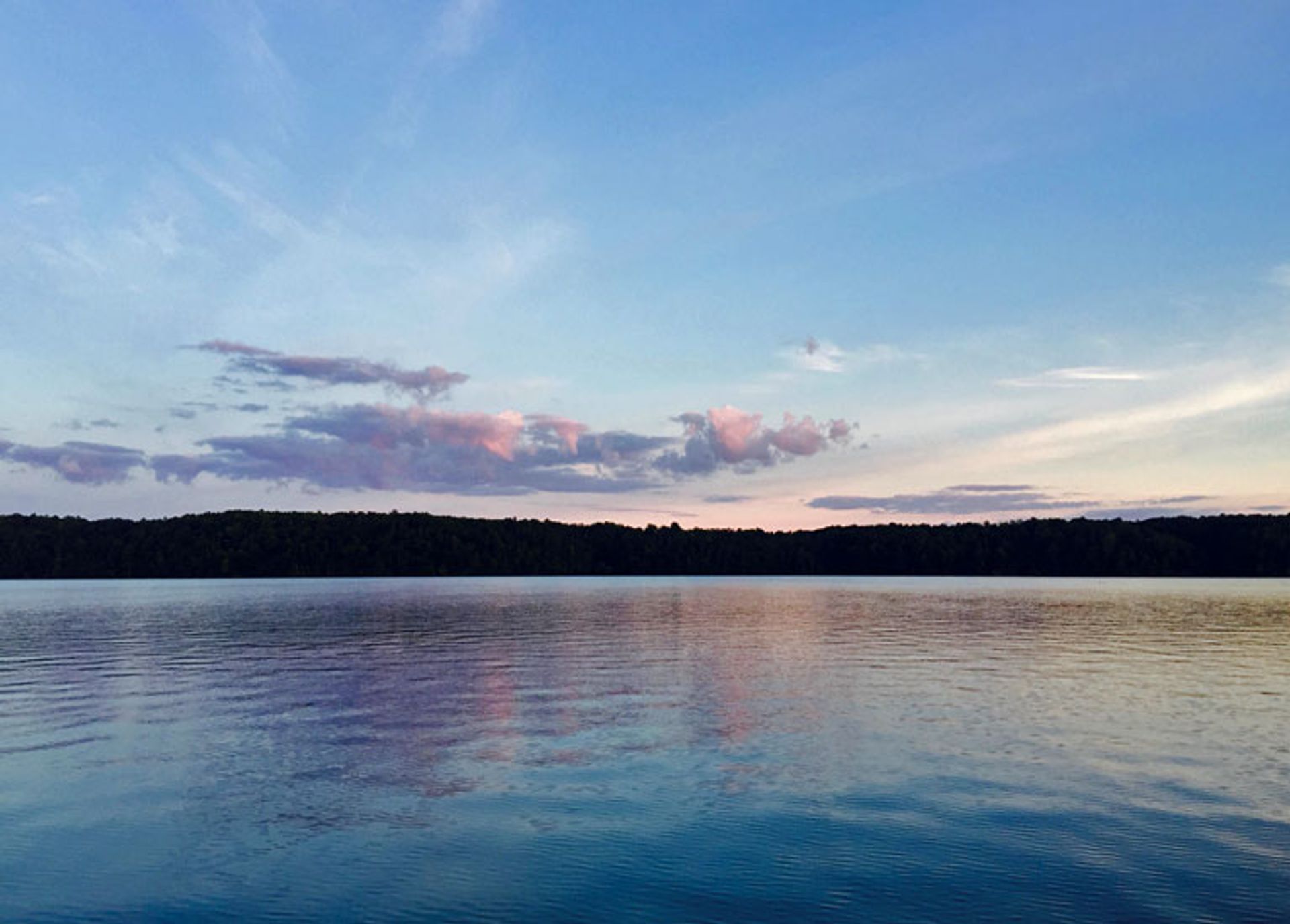 Northern Exposure Campground: A serene lake at sunset, with calm waters reflecting a colorful sky and distant trees lining the shore.