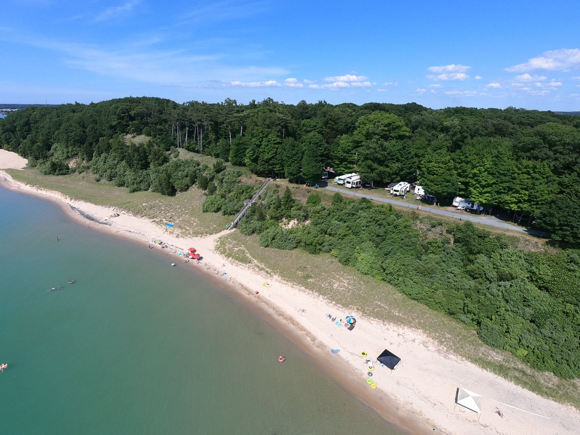 Buttersville Campground: A serene beach scene with clear water, sand, and greenery, featuring people enjoying the sun and camping nearby.