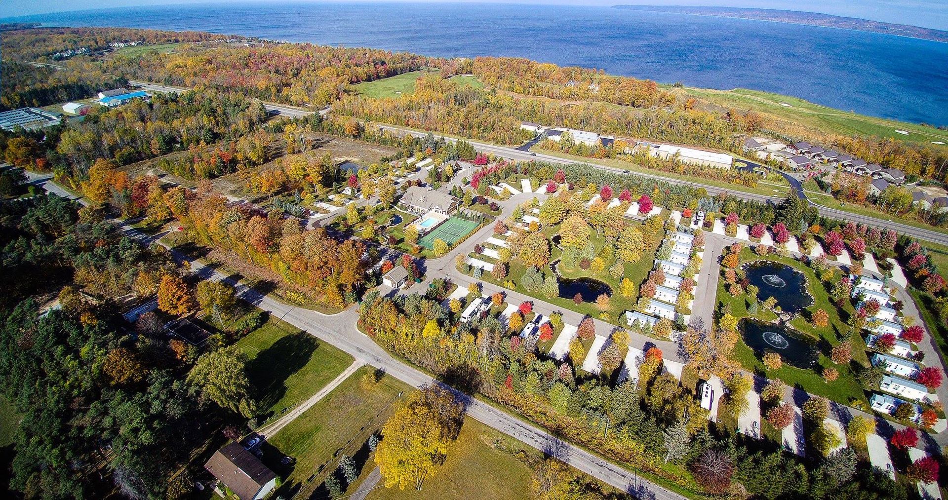 Sun Outdoors Petoskey Bay Harbor: Aerial view of a scenic landscape featuring colorful autumn foliage, a lake, and a residential area near the water.