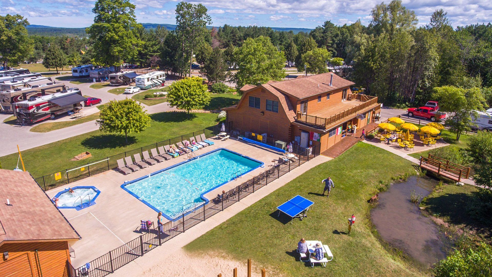 Yogi Bear's Jellystone Park™ Camp-Resort: Petoskey: Aerial view of a rustic lodge with a swimming pool, picnic area, and RV park surrounded by trees and grassy space.